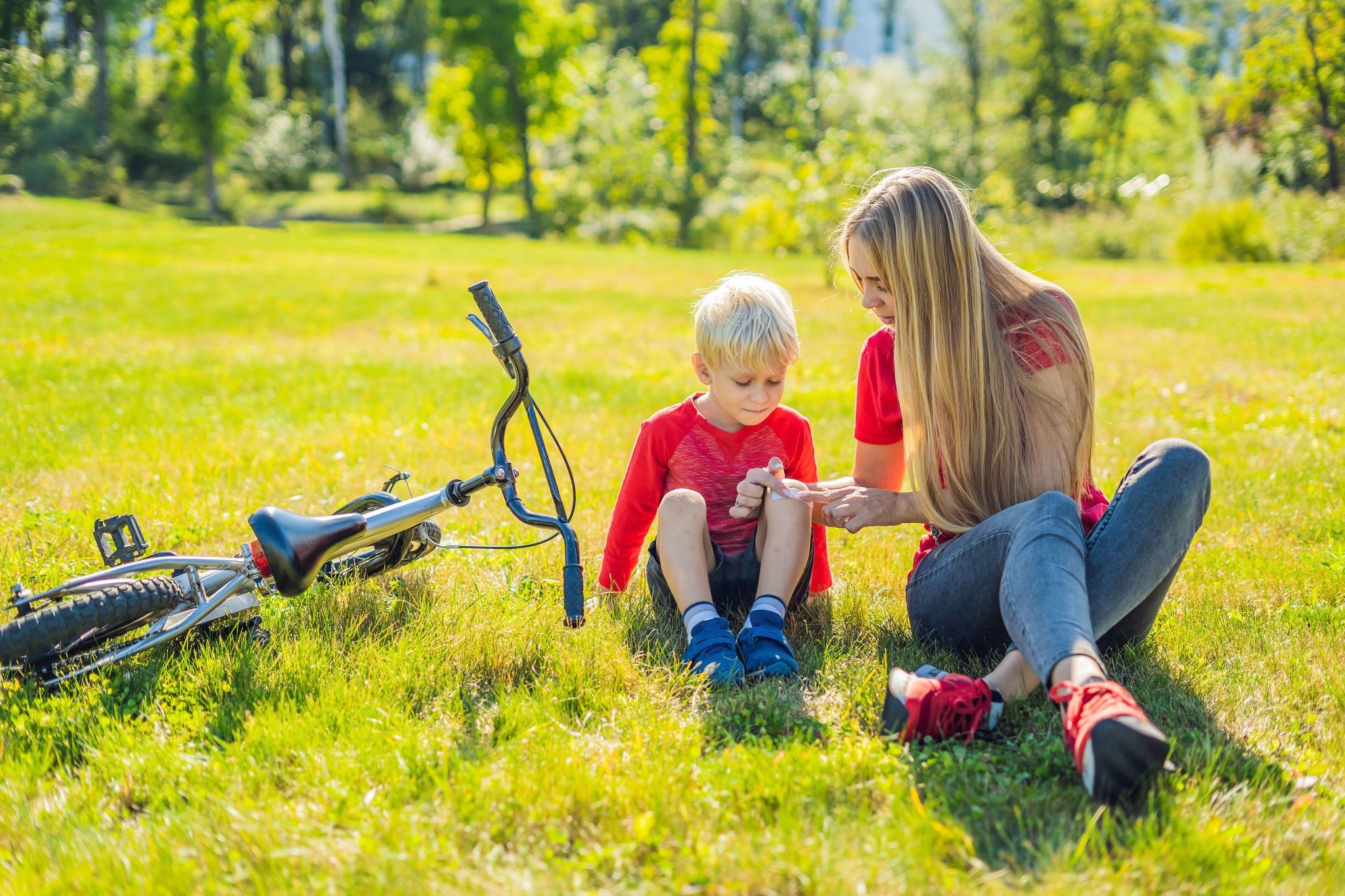 The boy fell off the bicycle, his mother pastes a plaster on his knee.